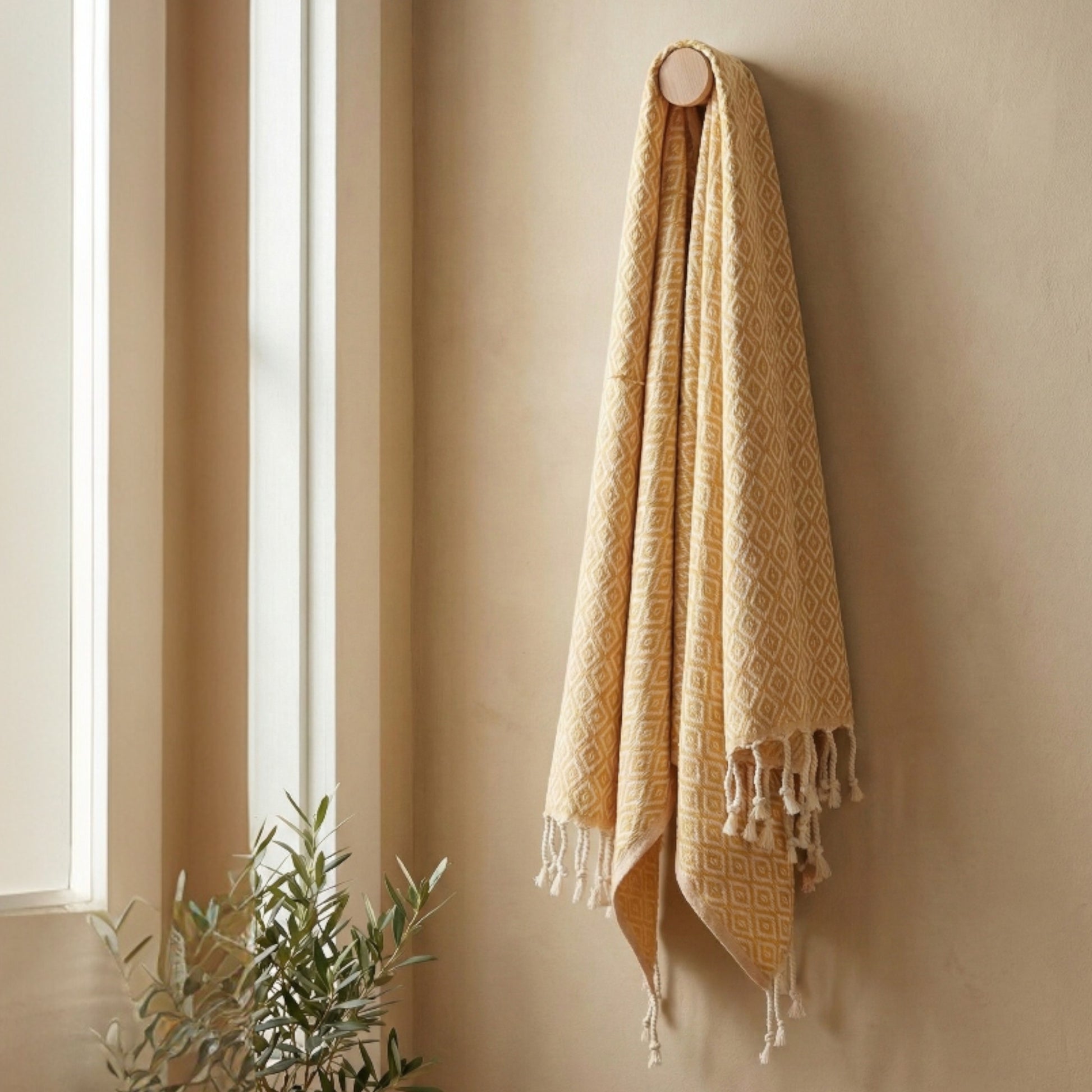Beige Diamond Design Turkish Hand Towel  Handwoven Natural Cotton Sustainable Anatolian Craft with tassels hanging on a beige wall next to a window.