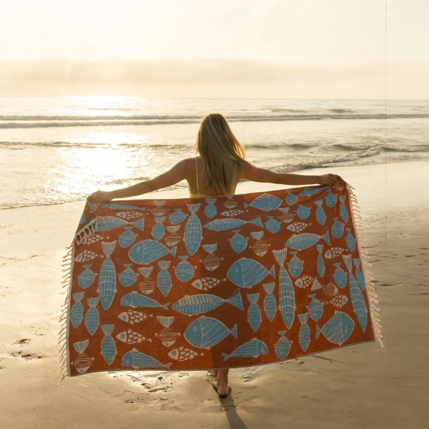 Woman holding a Fish Pattern 3-Layer Turkish Towel – Jacquard Woven Muslin Beach Towel on a sandy beach