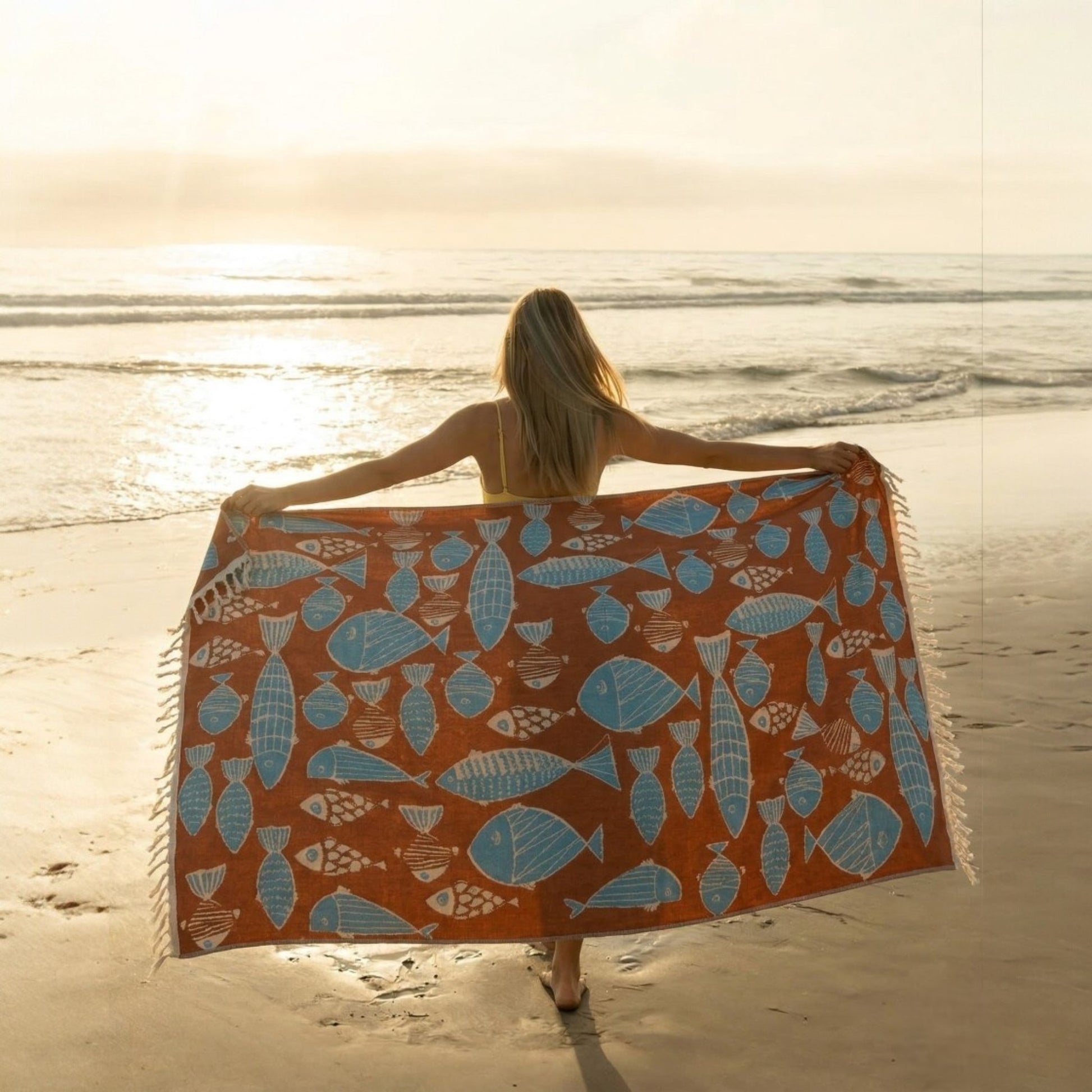 Woman holding a Fish Pattern 3-Layer Turkish Towel – Jacquard Woven Muslin Beach Towel on a sandy beach