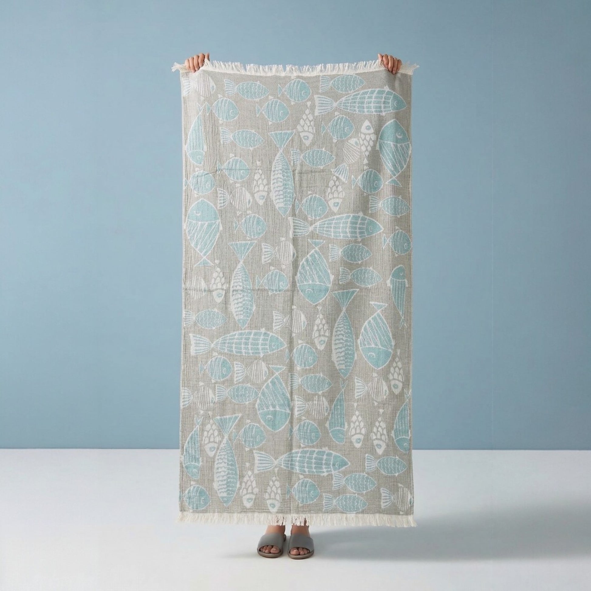 Person holding a Fish Pattern 3-Layer Turkish Towel – Jacquard Woven Muslin Beach Towel against a blue background