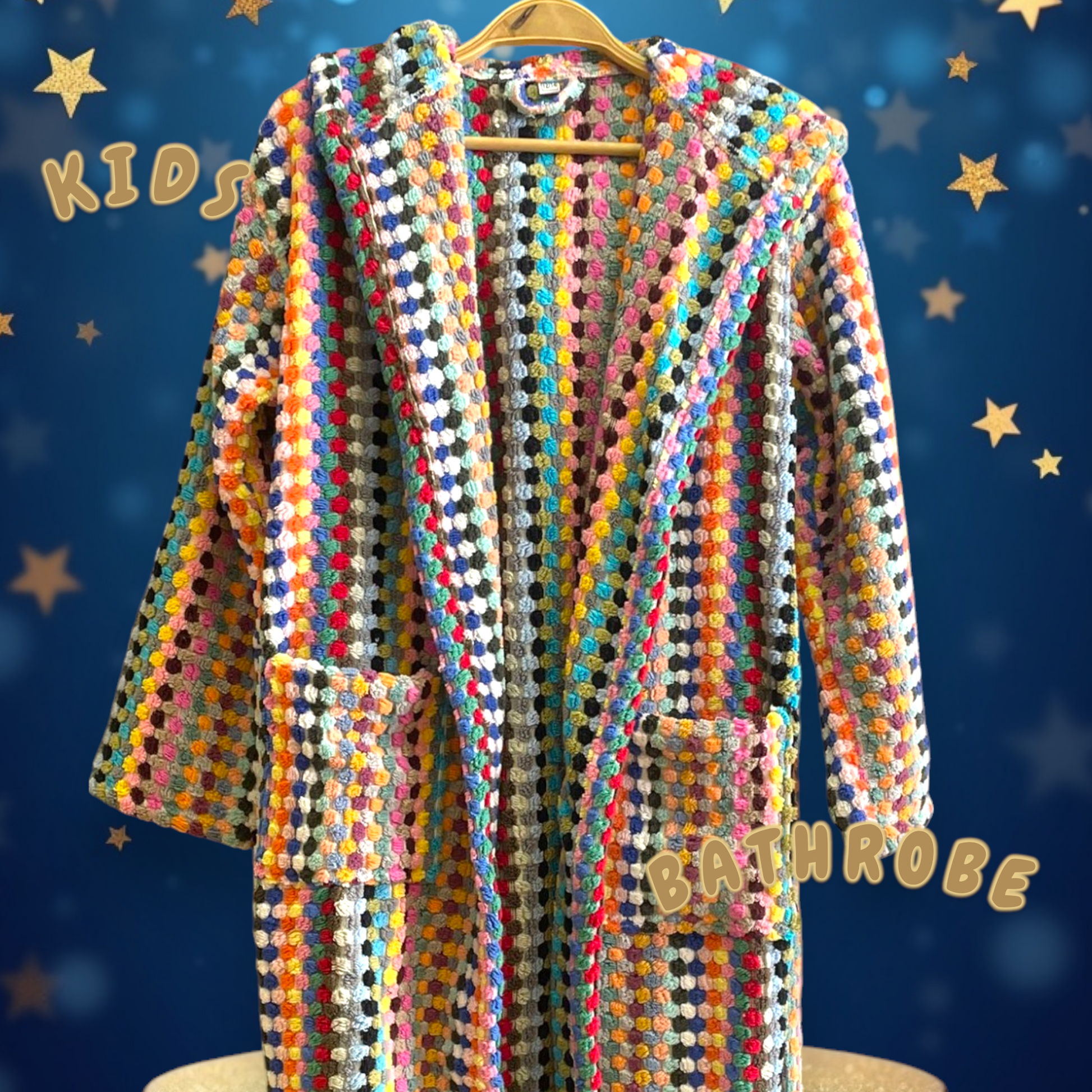 A colorful kids' bathrobe with geometric patterns and pompom details, displayed on a hanger with a blue background and star decorations.