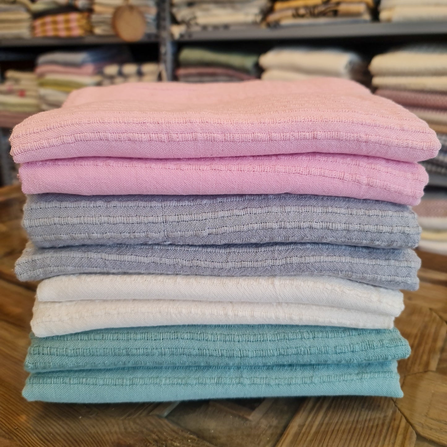 A selection of folded Turkish towels in various colors, including pink, gray, blue, and white, displayed on a wooden surface.