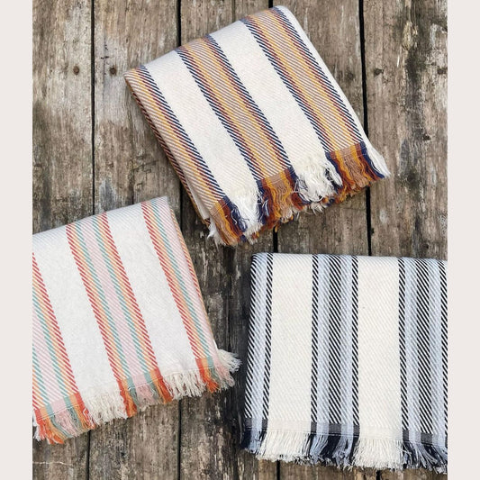 Three folded Natural Cotton Turkish Towels Pestemals with ecru bases and multicolored stripes, displayed on a wooden surface.