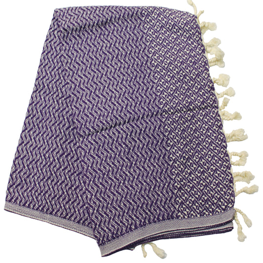 A purple Turkish towel with a geometric pattern and tassels on the end, laid out on a plain background.